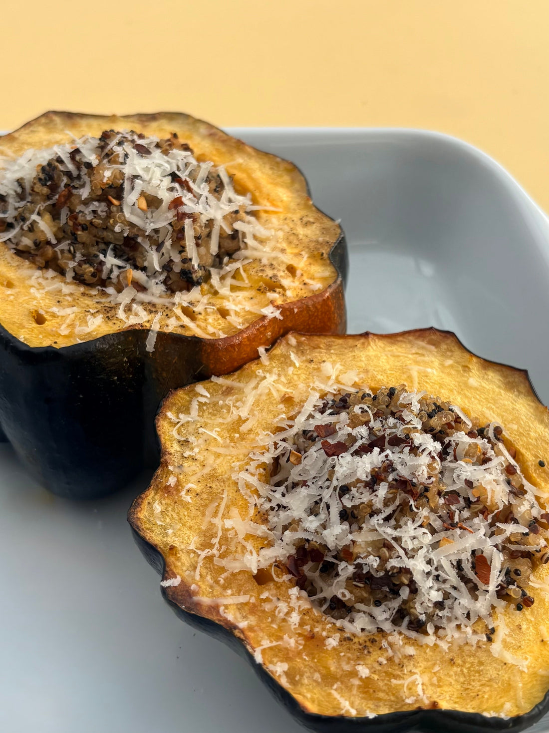 Stuffed acorn squash served in a white oven dish on a yellow table.
