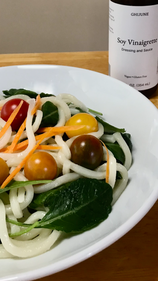 A plate of kale, shredded carrots, cherry tomatoes and noodles with a bottle of condiment