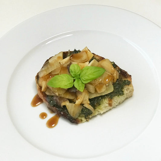 A plate of toast with pesto, sauteed onions and mushrooms, drizzled with sauce and garnished with basil