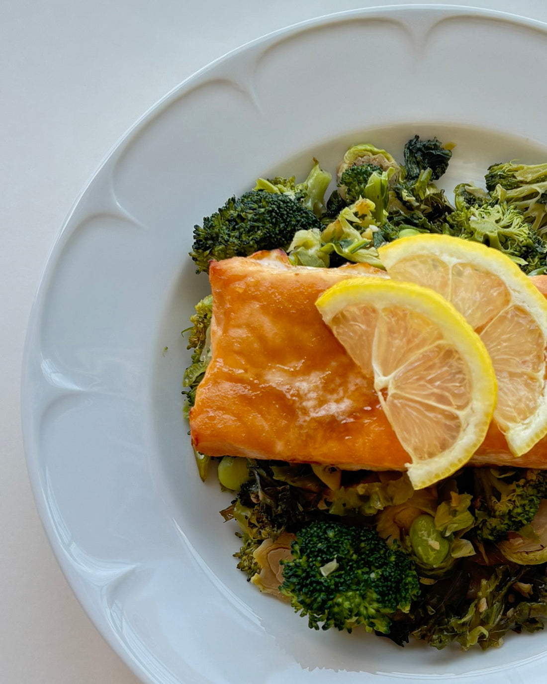 Butter-baked salmon fillet served over roasted vegetables with fresh lemon slices. The salmon is golden and flaky, resting on a colorful mix of roasted vegetables for a fresh, wholesome meal.