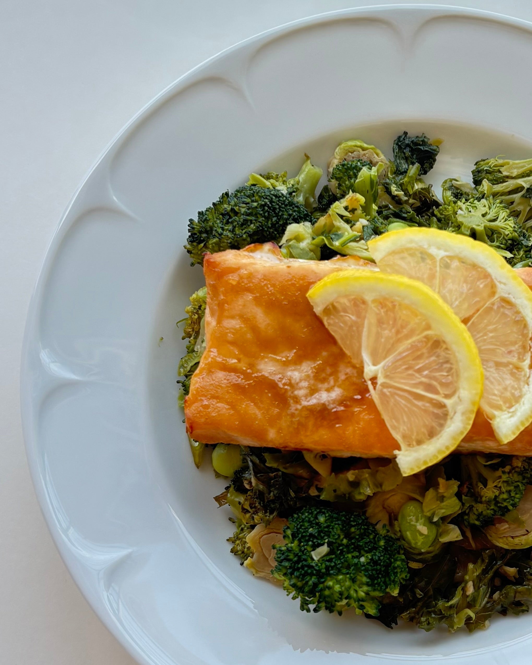 Butter-baked salmon fillet served over roasted vegetables with fresh lemon slices. The salmon is golden and flaky, resting on a colorful mix of roasted vegetables for a fresh, wholesome meal.