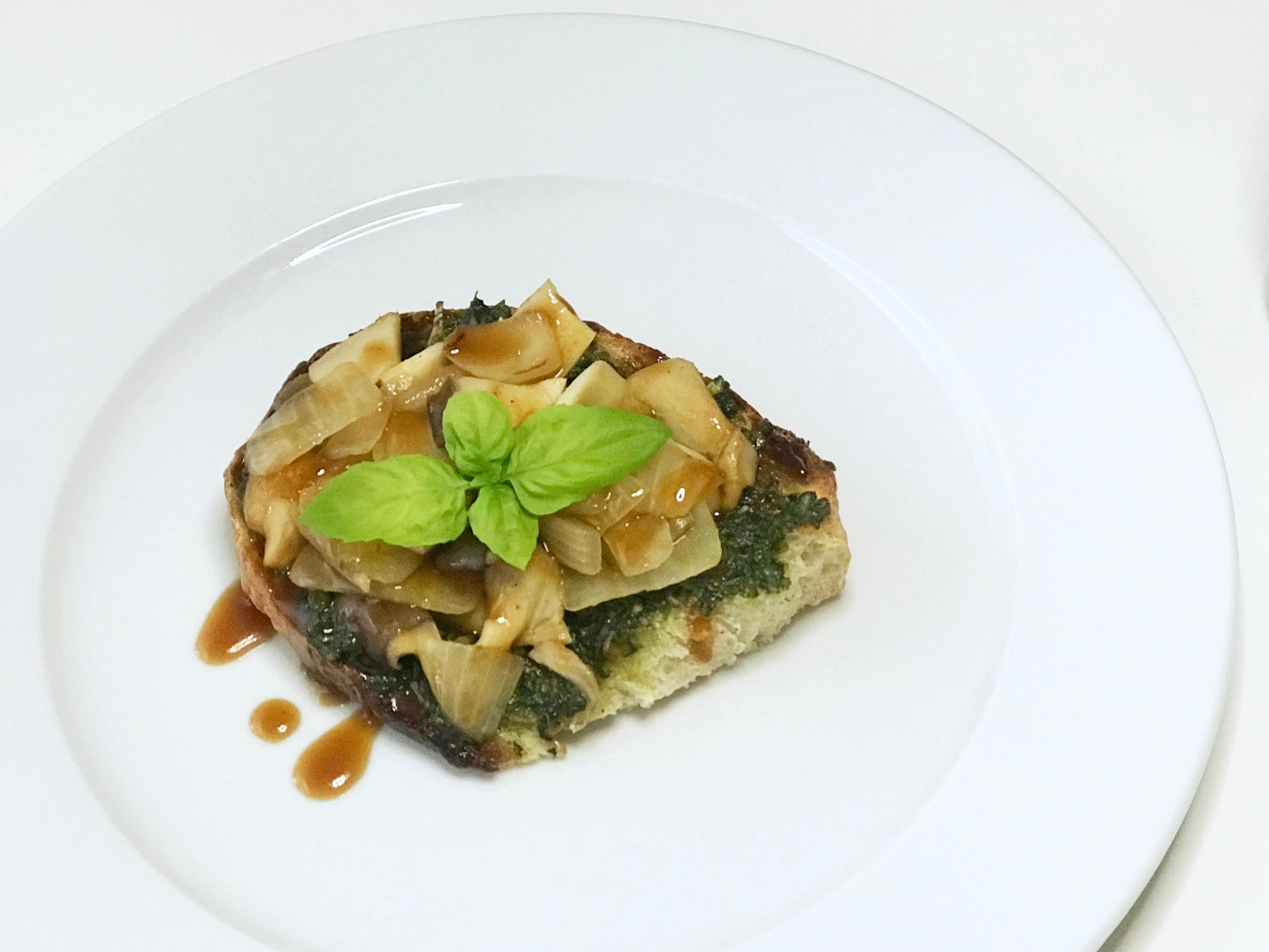 A slice of toasted sourdough topped with pesto, sautéed mushrooms and onions, and drizzled with GHIJUNE Soy Vinaigrette Dressing & Sauce. Fresh basil leaves garnish the toast, adding a vibrant green finish to the savory dish.
