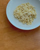 Video showing plain pasta noodles in a white bowl as a rich sauce is slowly drizzled over the top.